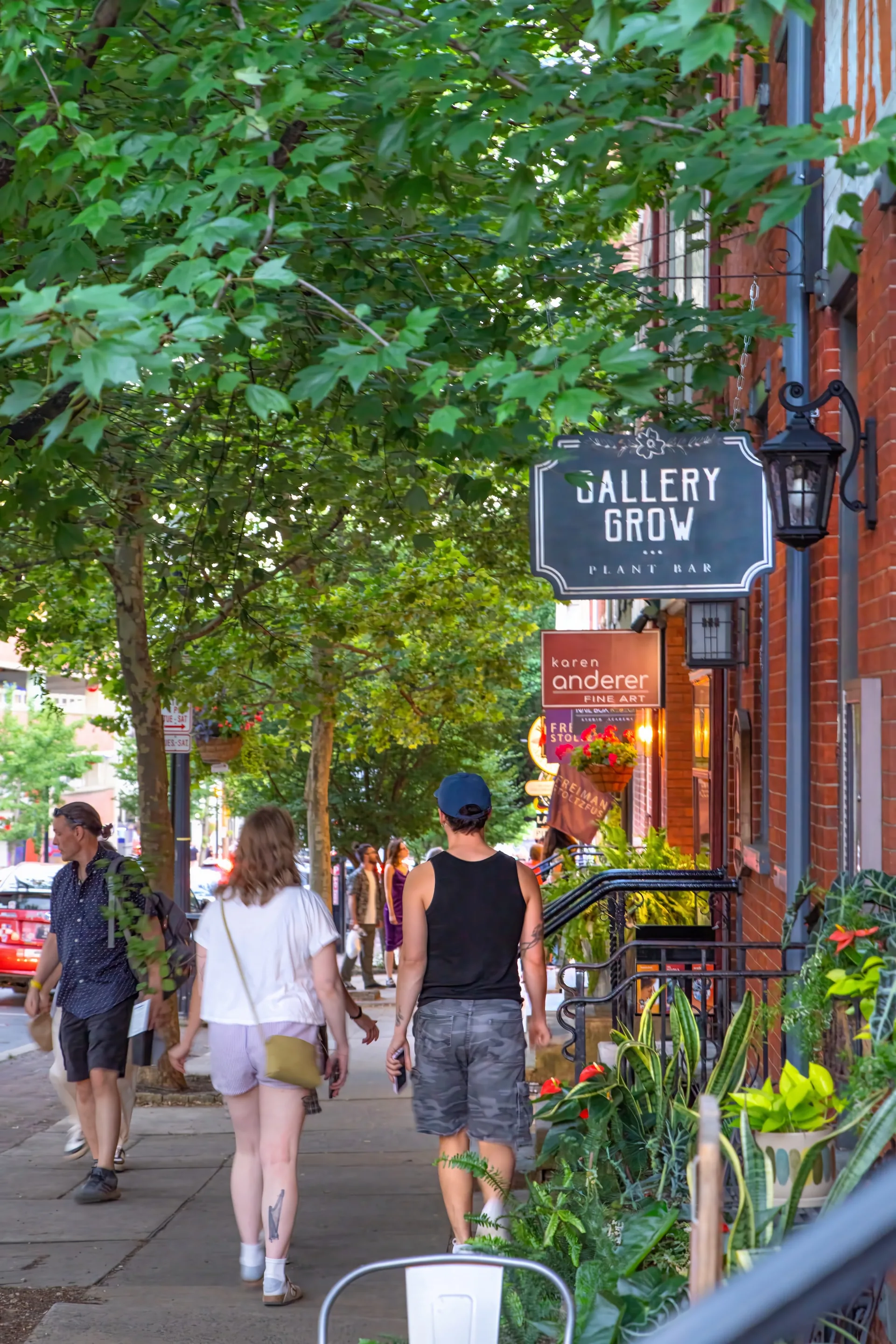 People walking along a leafy Lancaster sidewalk past independent gallery storefronts