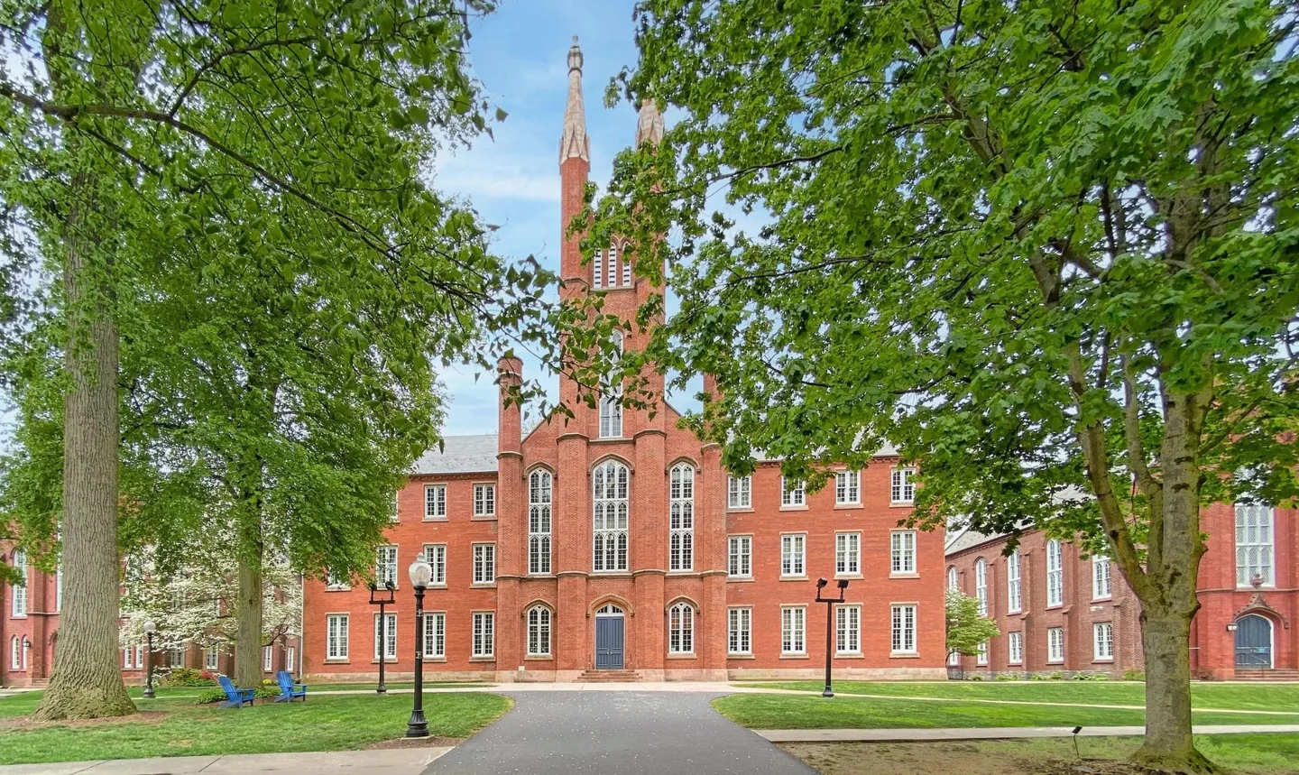 Red-brick building with a tall central tower framed by leafy trees
